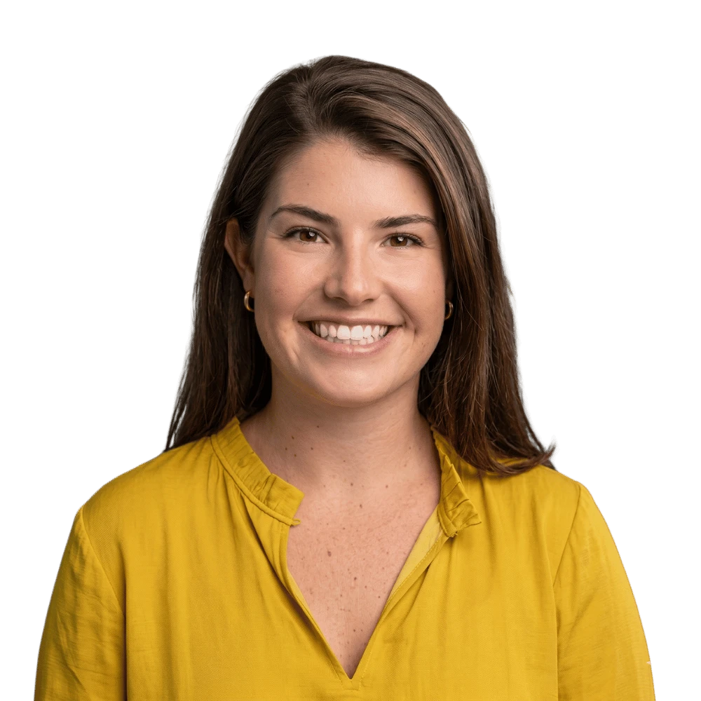 A smiling woman with brown hair wearing a mustard yellow blouse, photographed against a plain white background.